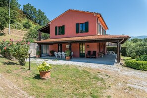 Una casa de dues plantes amb un porxo cobert, espai per seure a l'exterior i un jardí.