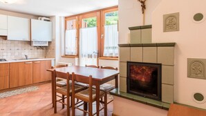 Une cuisine avec des meubles en bois, une table à manger avec des chaises, une cheminée et un crucifix accroché au mur.