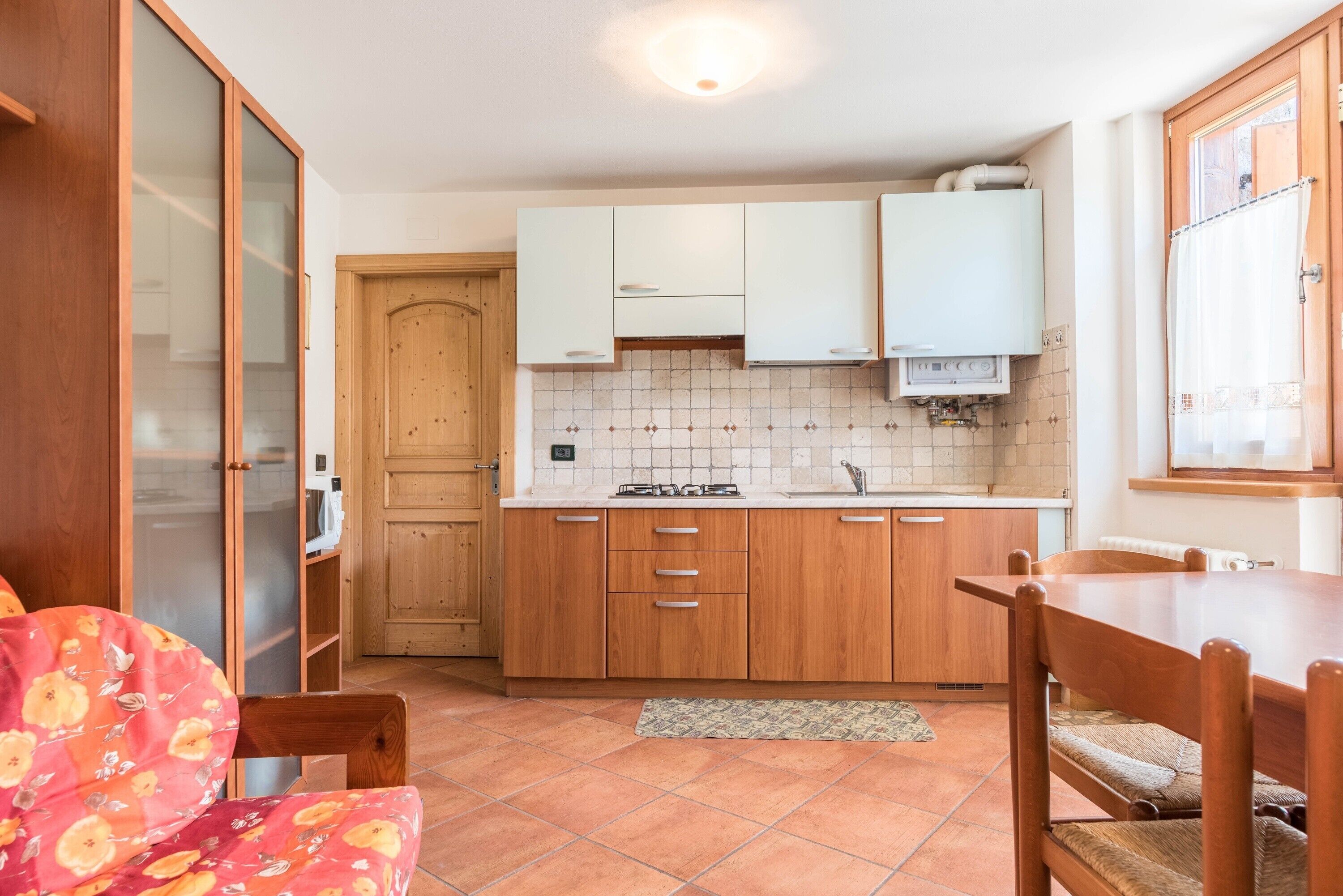 Una cucina compatta con mobili in legno, zoccolo in piastrelle e zona pranzo con tavolo e sedie.