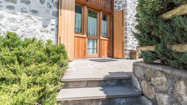 Un bâtiment en pierre avec une porte en bois, des marches en pierre et un petit banc en bois.