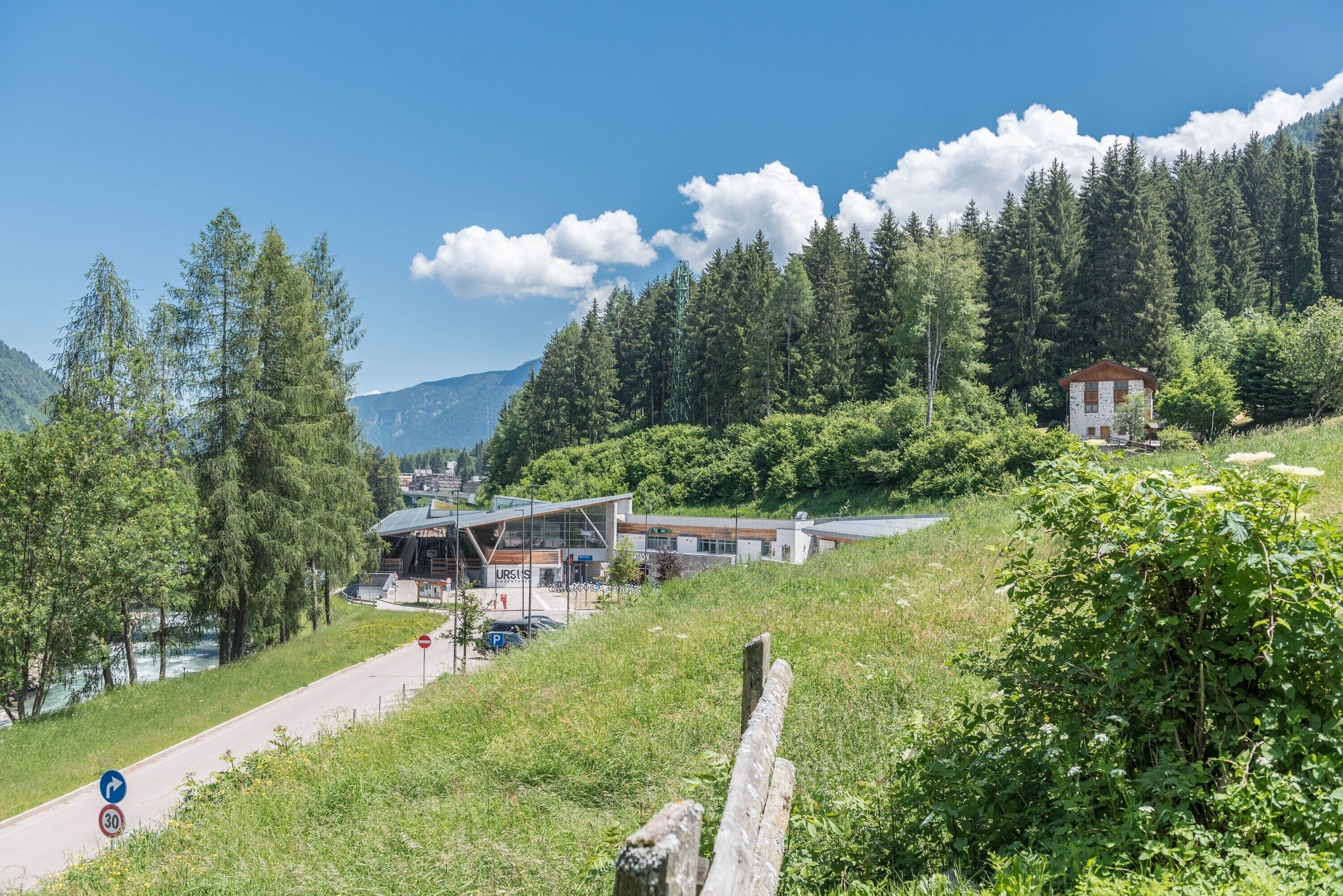 Un bâtiment moderne à la façade de verre, entouré d’une végétation luxuriante et de montagnes.