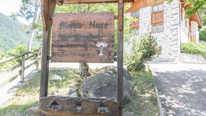 Une enseigne en bois portant les inscriptions « Maso Noce » et « Haus Maggimitt », fixée à une structure en bois, avec un bâtiment en pierre en arrière-plan.