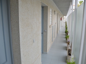 A corridor with a speckled wall, tiled floor, and potted plants along the right side.