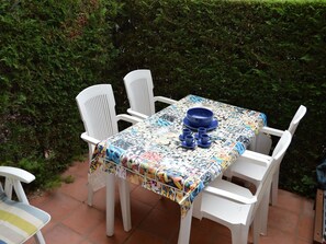 A patio table with a colorful tablecloth, white chairs, and blue tableware.