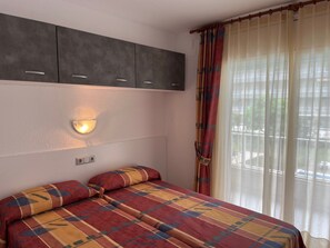 A bedroom with a bed, a wall-mounted light, and a window with curtains.