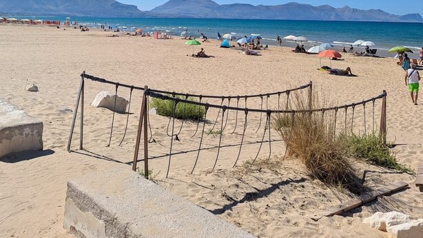 Ein Strand mit einem Seilsperrung, blauem Himmel und Bergen im Hintergrund.