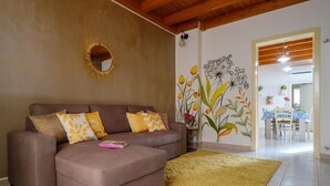 A living room with a brown sofa, yellow and white patterned pillows, a yellow rug, a wall mural, and a dining area in the background.