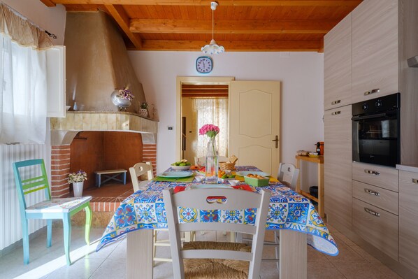 A dining area with a table set for two, a wooden ceiling, and a kitchen with a stove and oven.
