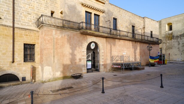 A historic building with a stone facade, an arched entrance, and a balcony with wrought iron railings.