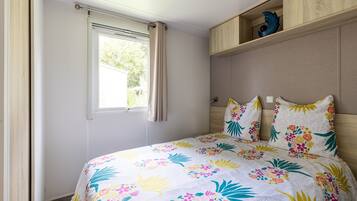 A bedroom with a bed, a window with curtains, a wooden shelf with decorative items, and a headboard.