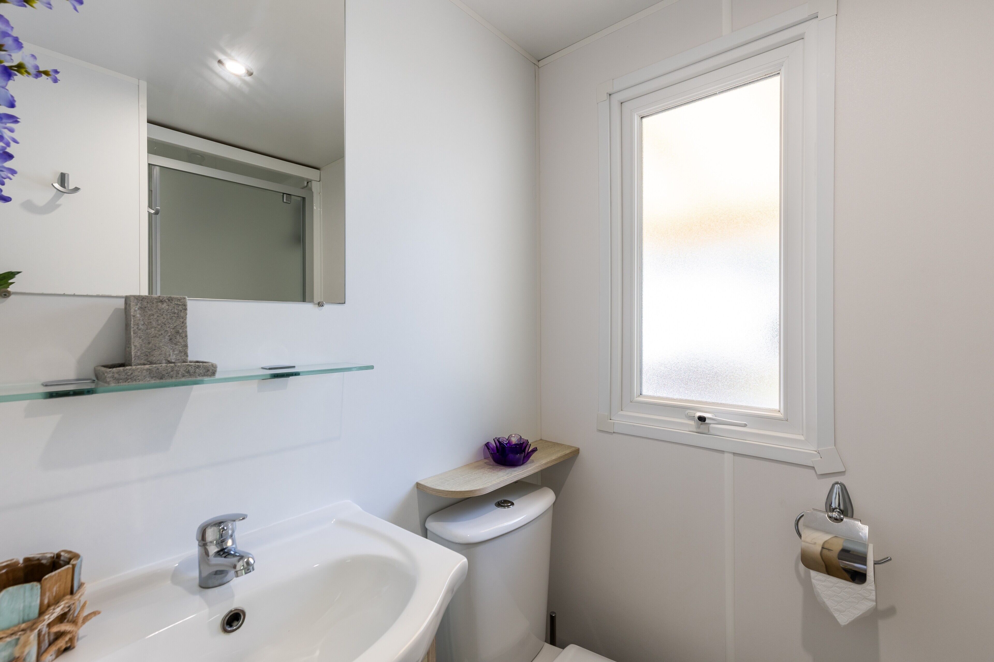 Un bagno con un lavandino bianco, uno specchio, un water, una finestra e un porta asciugamani.