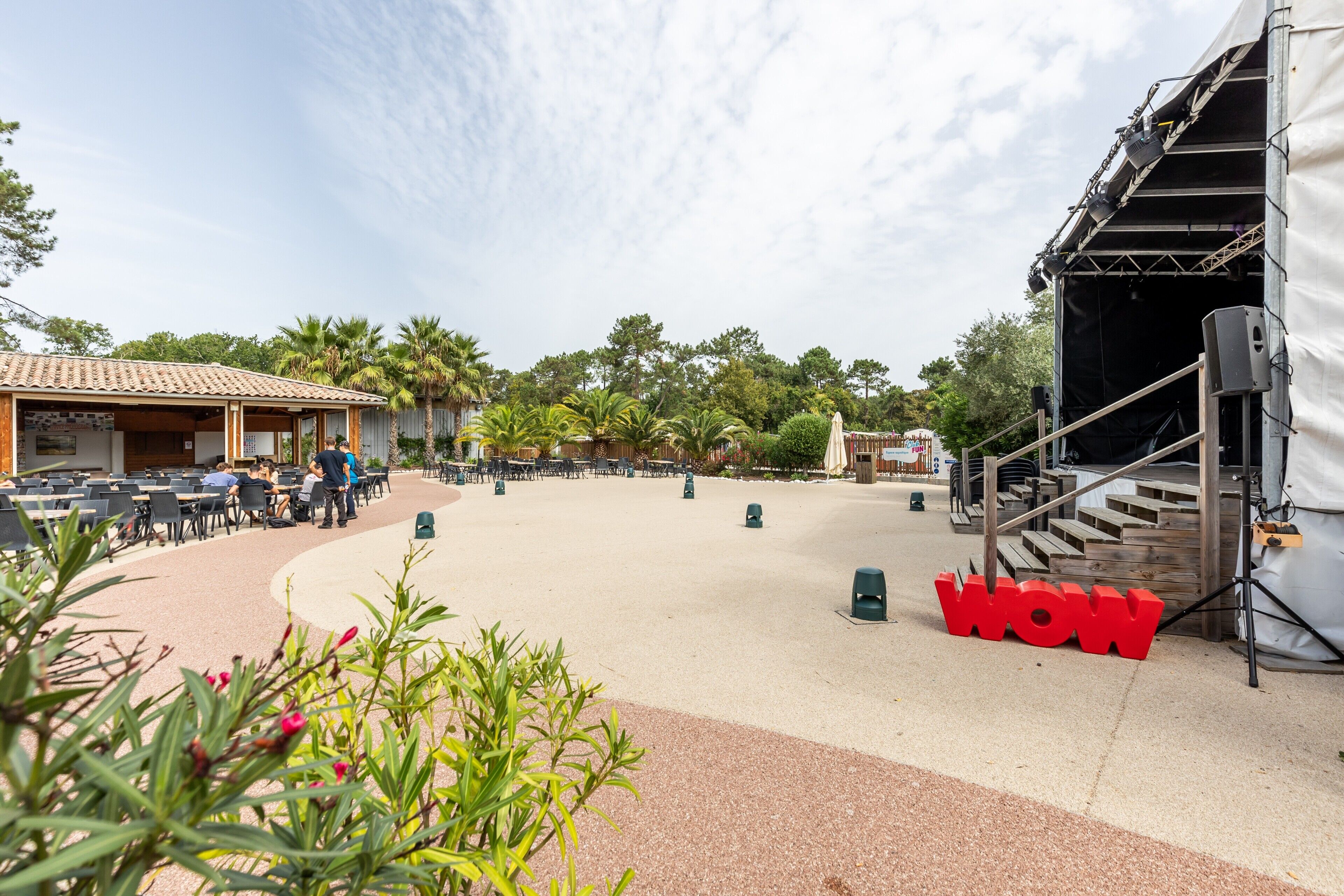 An outdoor seating area with tables and chairs, a stage with speakers, and a 'WOW' sign.