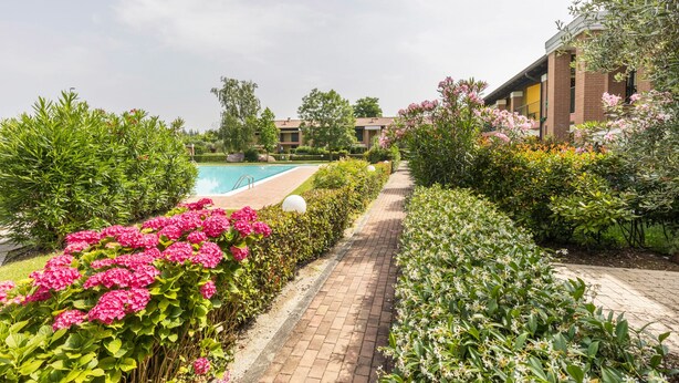 Un percorso che conduce a una piscina circondata da vegetazione lussureggiante e piante fiorite.