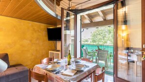 Zona pranzo con tavolo apparecchiato per quattro persone, divano e televisore a parete.