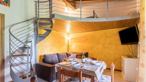 Una scala a chiocciola, un'area pranzo con tavolo apparecchiato per due, un divano e una televisione appesa al muro.