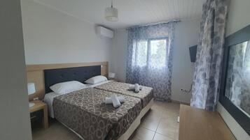 Habitación de hotel con dos camas, cabecero de madera, ventana con cortinas, mesita de noche con lámpara y televisor de pantalla plana montado en la pared.