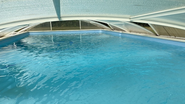 En swimmingpool med kristallklart blått vatten, omgiven av ett överbyggt område med ett välvt tak.