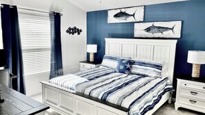 Um quarto com cama, mesas de cabeceira, escrivaninha e janela com cortinas.
