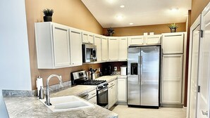 Uma cozinha moderna com armários brancos, eletrodom ésticos de aço inoxidável e bancada de mármore.