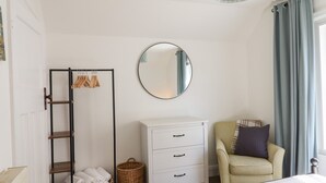 A bedroom with a bed, a white dresser, a chair, a mirror, a wardrobe, and a hanging light fixture.