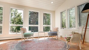 A sunlit room with large windows, a round rug, and two chairs with cushions. - Luxe Cape Cod Farmhouse. Walk to Ellis Landing Beach! (Brewster)