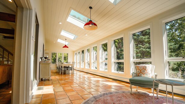 A spacious room with large windows, a wooden floor, and a dining area with a table and chairs. - Luxe Cape Cod Farmhouse. Walk to Ellis Landing Beach! (Brewster)