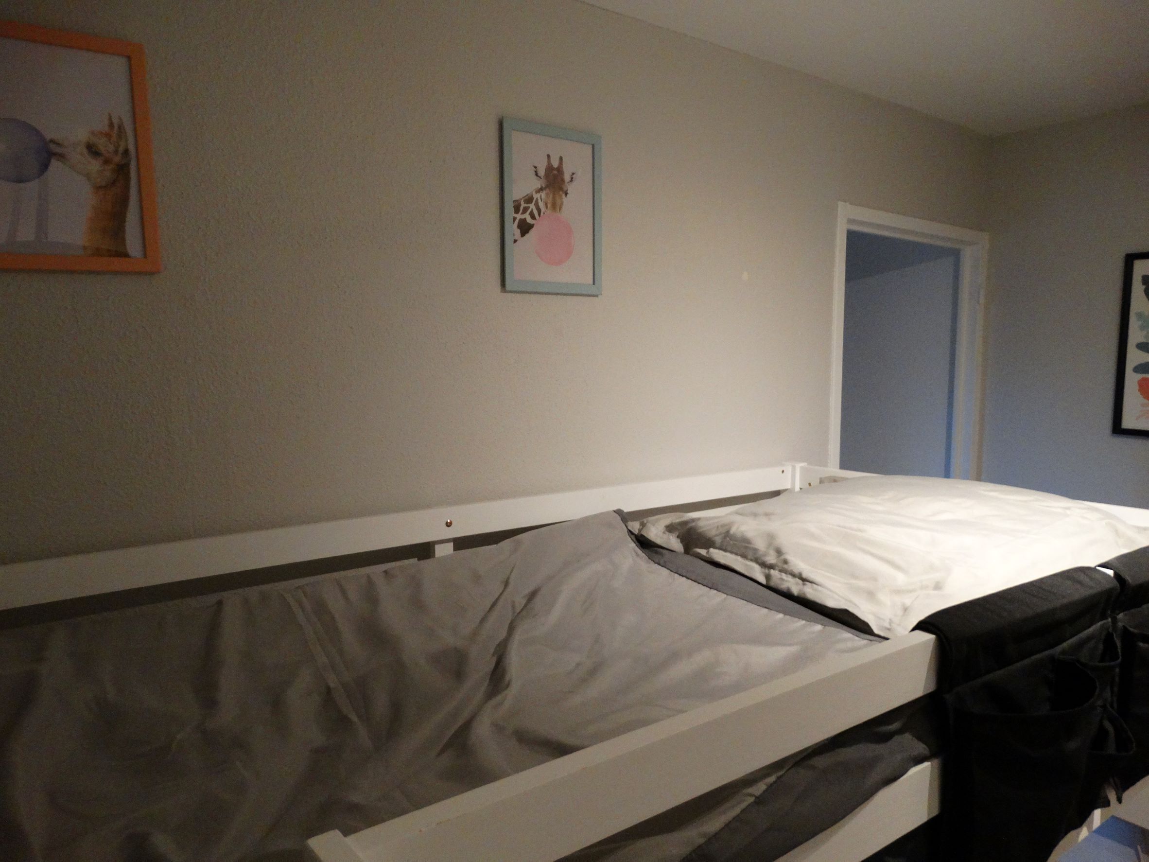 A single bed with a grey mattress and white bedding in a room with plain walls.
