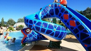 A water slide with a blue and green design, surrounded by a pool area with people enjoying the water. - Kleines Haus mit Garten, Ideal für Ruhe, Meer, Funboarding und Windsurfing (Le Barcarès)