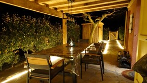 An outdoor patio with a long table and chairs, surrounded by stone flooring and a wooden pergola. - Kleines Haus mit Garten, Ideal für Ruhe, Meer, Funboarding und Windsurfing (Le Barcarès)