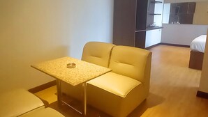 A small, modern room with a single bed, a small table, and a sofa. - Hotel Aruni Ancol (Jakarta)