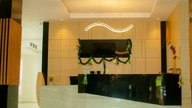 A reception area with a black reception desk, a flat-screen TV mounted on the wall, and a curved light fixture above. - Hotel Aruni Ancol (Jakarta)