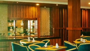 A restaurant with wooden paneling, green upholstered chairs, and a glass display case in the background. - Hotel Aruni Ancol (Jakarta)