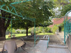 Une cour avec un jeu d’échecs, une table, des chaises et une structure en forme de pergola.