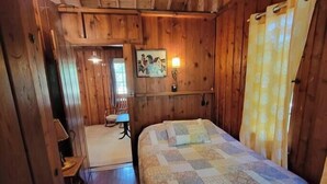 Een houten slaapkamer met een bed, een stoel, een tafeltje en een schilderij aan de muur.
