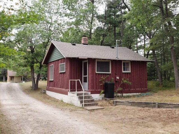 A small, single-story cabin with a red exterior and a green roof, surrounded by trees. - Sage, Mermaid Coast Cottages on Lake Huron (East Tawas)