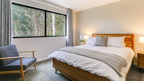 Een slaapkamer met een groot bed, een stoel, een nachtkastje en een raam met gordijnen.