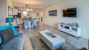 A modern living room with a sofa, coffee table, TV, and a dining area with chairs and a table. - 205 Luxury condo at Storey lake (Kissimmee)