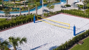 A large sandy volleyball court with blue and yellow boundary lines, surrounded by greenery and a pool area. - 205 Luxury condo at Storey lake (Kissimmee)