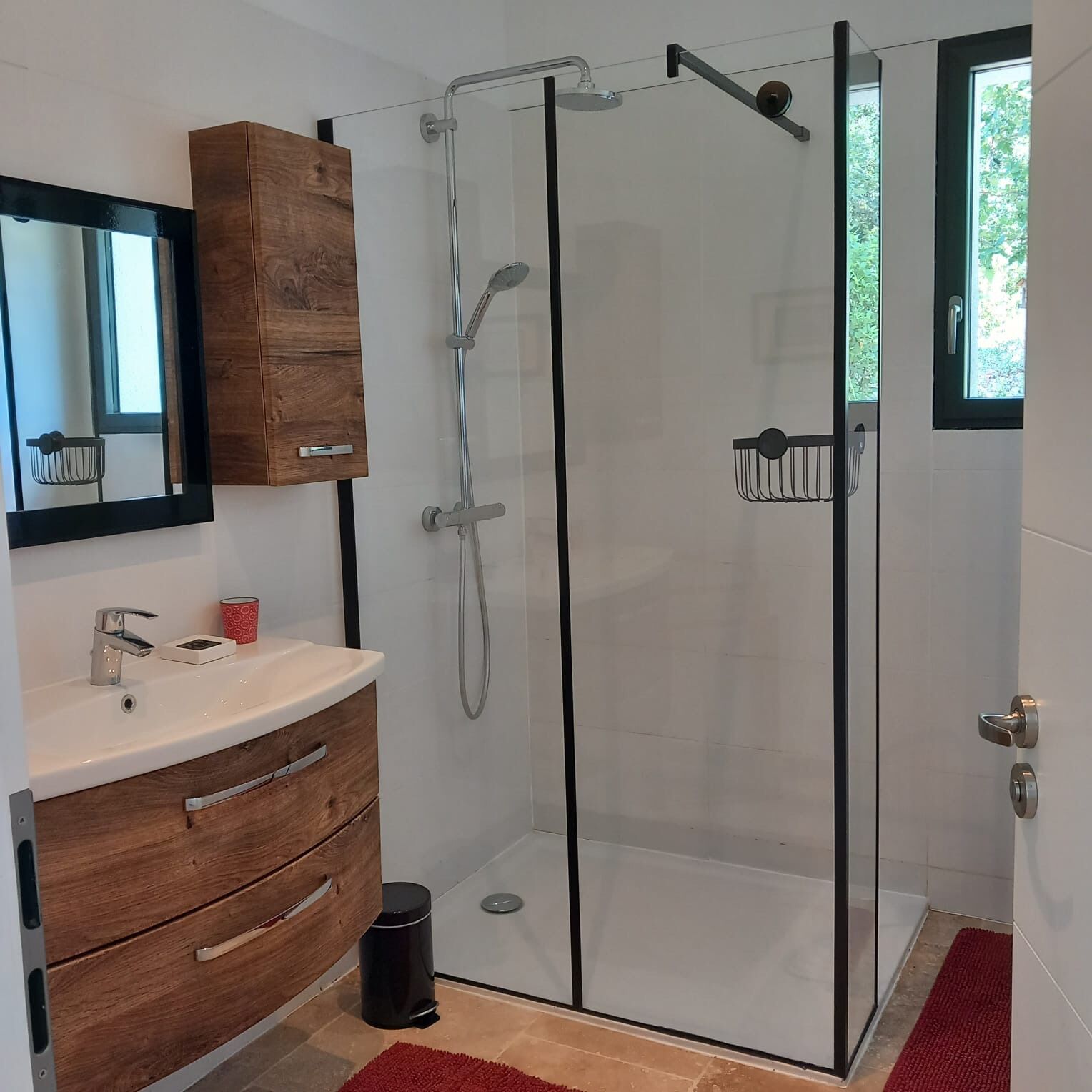 A modern bathroom with a glass shower enclosure, a wooden vanity, and a large mirror.