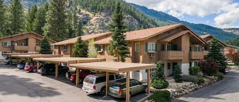 A row of wooden cabins with attached parking, set against a mountainous backdrop.