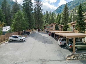 Un estacionamiento con varios autos, un edificio con un porche cubierto y un telón de fondo de montaña boscosa.