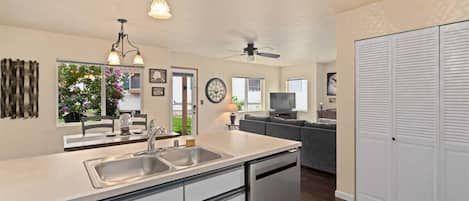 A modern kitchen with a dishwasher, a dining area with a table and chairs, a living room with a sofa, and a large closet.