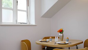 Ein Essbereich mit einem runden Tisch, vier Stühlen, einer Blumenvase und einem Fenster mit Jalousien.