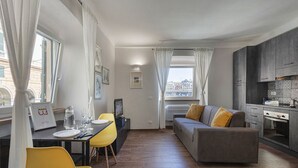 A modern living room with a sofa, dining table, and chairs. There is a kitchen area with cabinets and a stove. - San Lorenzo View Apartment 4 by Wonderful Italy (Genova)