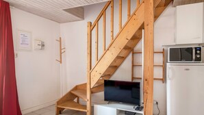 A compact living space with a wooden staircase, a flat-screen TV, a white refrigerator, and a small cabinet. - House in the historic center of Pornic (Pornic)