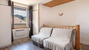 A bedroom with a wooden headboard, a bed with a grey and white duvet, a window with curtains, and a radiator on the wall. - House in the historic center of Pornic (Pornic)