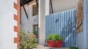 A narrow alleyway with a blue wooden gate, a red brick wall, and a small garden area with potted plants. - House in the historic center of Pornic (Pornic)