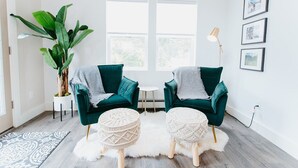 Una sala de estar moderna con dos sillones color turquesa, una mesita redonda pequeña, una planta grande en maceta y una alfombra blanca.