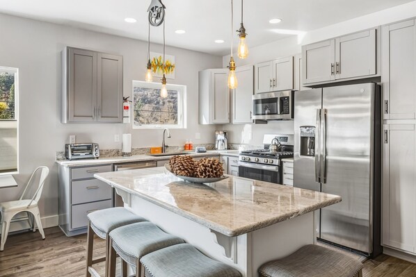A modern kitchen with stainless steel appliances, a marble island, and pendant lighting.
