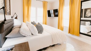 Un dormitorio moderno con cama, ventilador de techo, televisión y cortinas amarillas.